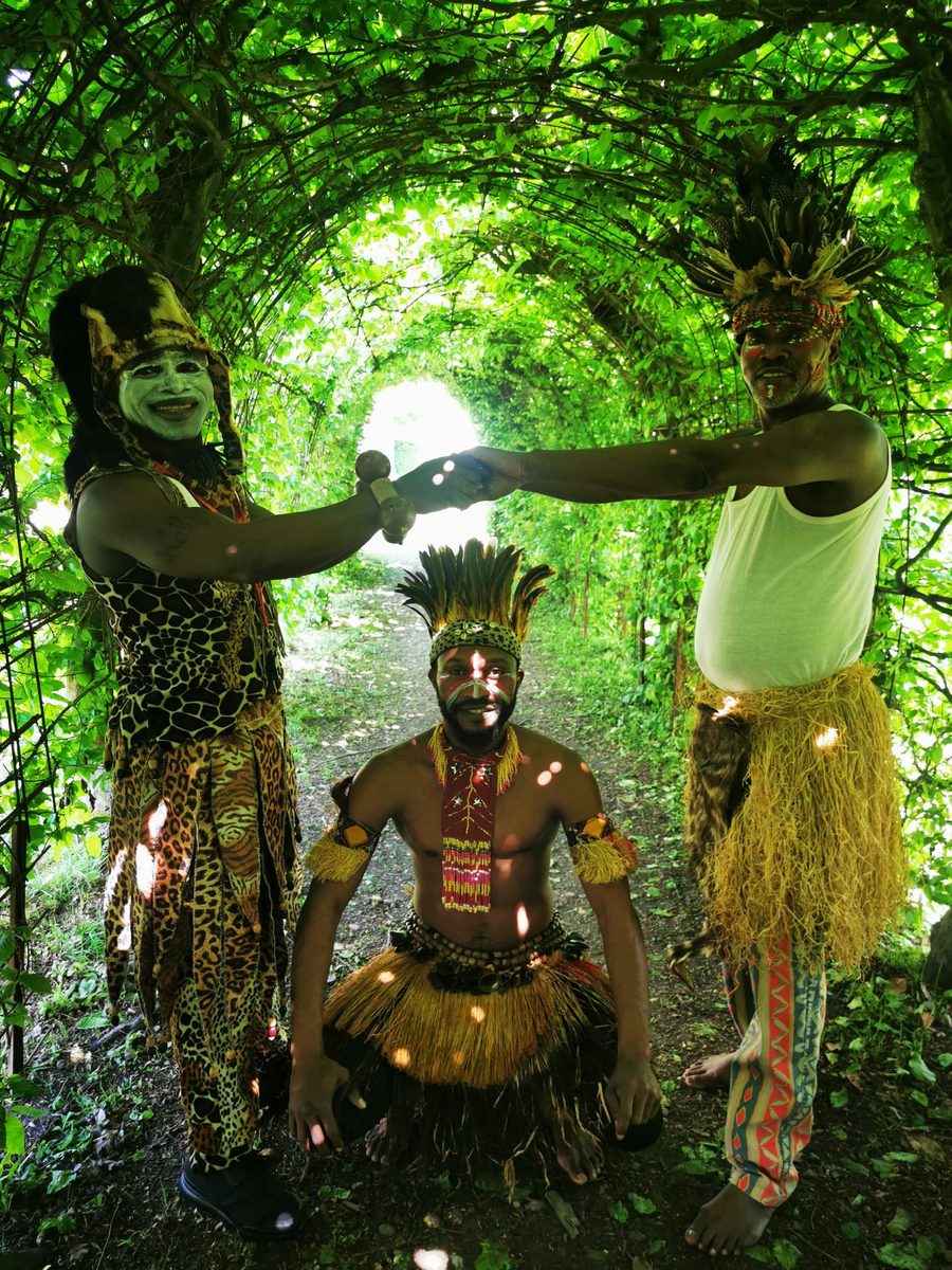Three Groupe Furaya performers in a green outdoor setting